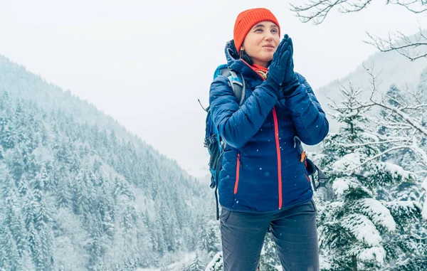 バックパックを着た女性バックパッカーは 冬の山岳森林ルートをトレッキングしながら ヤシの手を暖めて雪の山の風景を楽しんでジャケットを暖めています 自然概念の活動家 — ストック写真
