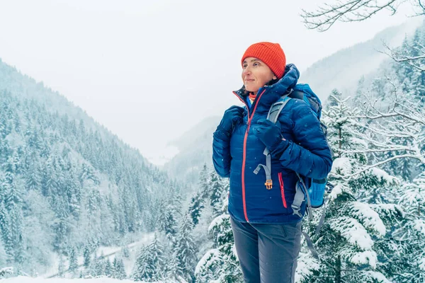 バックパックを着た女性のバックパッカーは 冬の山岳森林ルートをトレッキングしながら 雪の山の風景を楽しむジャケットを暖めていました 自然コンセプトのイメージで活躍する人たち — ストック写真