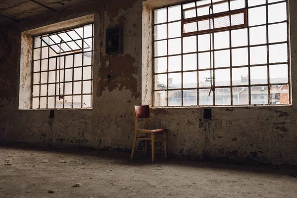 古いヴィンテージの壁に格子の広い窓が付いている古い工場の部屋を放棄しました 窓の近くの孤独な古い椅子 グランジイメージのコンセプトイメージ — ストック写真