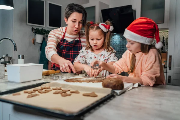 可爱的小女孩戴着红色的圣诞帽 妈妈在家里的厨房里一起用饼干切割机做自制面团圣诞姜饼 快乐的家庭假期准备 童年的概念 — 图库照片