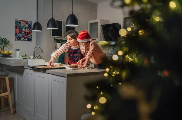 可爱的小女孩戴着红色的圣诞老人帽 妈妈在家里的厨房里一起用饼干切割机自制圣诞姜饼 快乐的家庭假期准备和童年的概念 — 图库照片