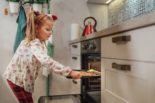 自家製の甘いビスケットを作る小さなかわいい女の子 彼女は熱いオーブンにベーキングシートを入れて クリスマスクッキーの準備 家庭の甘い家と暖かい家族の生活の瞬間のコンセプト — ストック写真