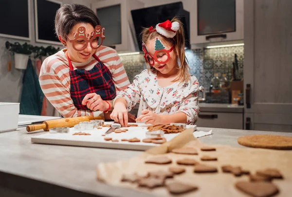 自家製生地を作る面白い眼鏡でお母さんとかわいい女の子クリスマスジンジャーブレッドクッキーホームキッチンで一緒にクッキーカッターを使用しています 幸せな家族の休日の準備 子供時代のコンセプト — ストック写真