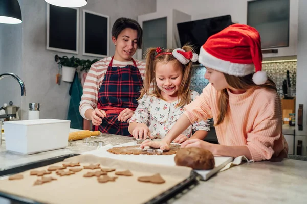 手作り生地を作る母親と赤いサンタの帽子のかわいい女の子クリスマスジンジャーブレッドクッキーホームキッチンで一緒にクッキーカッターを使用しています 幸せな家族の休日の準備 子供時代のコンセプト — ストック写真