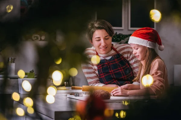 可爱的小女孩戴着红色的圣诞老人帽 妈妈在家里厨房里用滚动的别针一起做自制的圣诞姜饼 快乐的家庭假期准备和童年的概念 — 图库照片