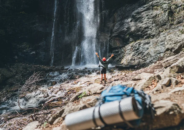 一个穿着活跃的步行服装站在山河瀑布边的女人站起来 享受着大自然的力量 背包在前景 远足的自然概念形象 — 图库照片