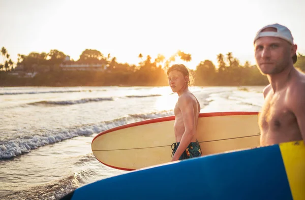 带着冲浪板的少年去冲浪 他有一个寒假 和他的父亲一起在斯里兰卡岛上享受着美丽的夕阳 家庭主动休假概念 — 图库照片