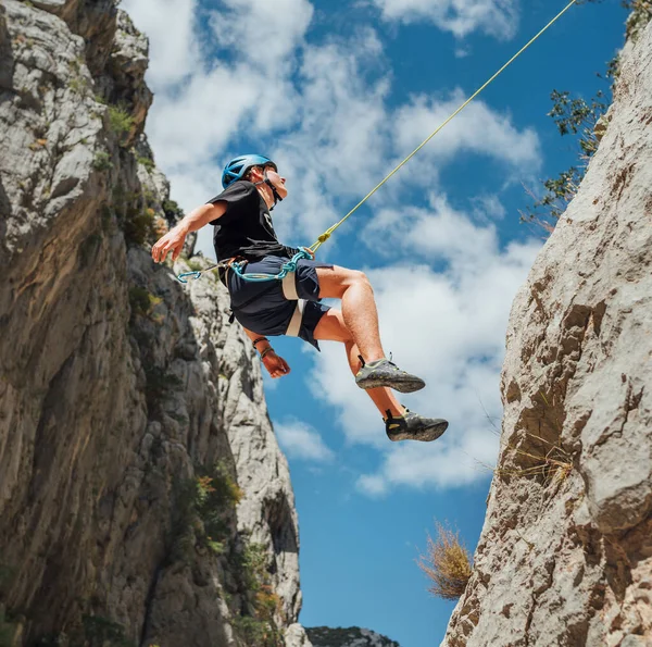 在克罗地亚的帕克里卡峡谷 一名戴着保护头盔的少年爬上了垂直的悬崖岩壁 用绳子环带装置 爬上了安全带 积极的极限运动时间概念 — 图库照片