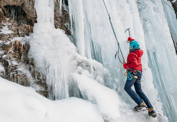 暖かい冬の登山服 安全ハーネス ヘルメットに身を包んだ氷の登山者は 2つの氷の登山軸とクランポンを使用して凍結滝を登る アクティブ人とスポーツ活動のコンセプトイメージ — ストック写真
