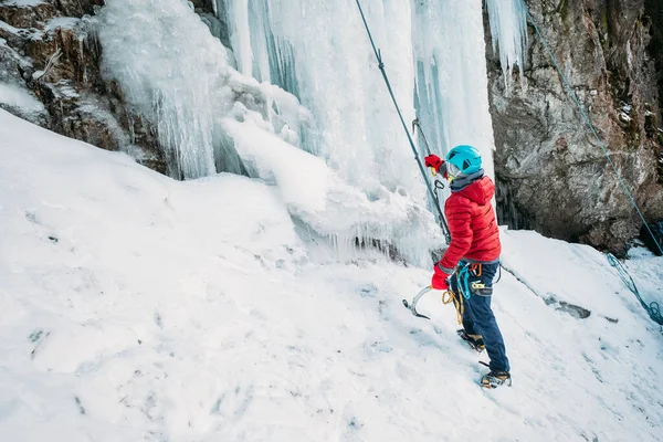 凍った滝の下に暖かい冬の登山服 安全ハーネスとヘルメットを身に着けていた氷のクライマー アクティブ人とスポーツ活動のコンセプトイメージ — ストック写真