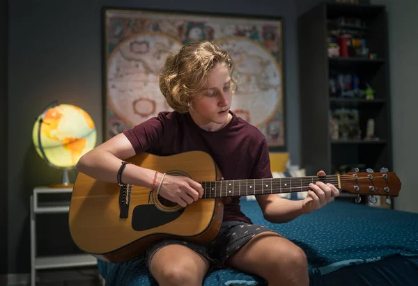 男孩儿坐在舒适的床上 穿着休闲装在家里孩子的房间里弹奏声吉他的肖像 音乐和自我教育概念形象 — 图库照片