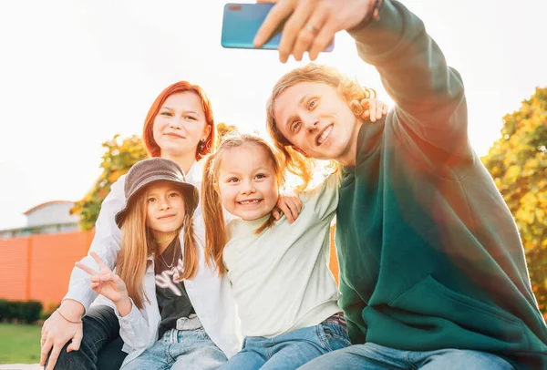 3人の笑顔の姉妹と弟の10代の肖像画は 現代のスマートフォンのカメラを使って自画像を撮る 不注意な若い十代と子供の頃の時間と近代的な技術の概念のイメージ — ストック写真
