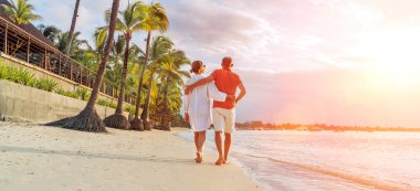 Couple in love hugging while walking on a sandy exotic beach. They have an evening walk by Trou-aux-Biches seashore on Mauritius island. People relationship and tropic honeymoon vacations concept