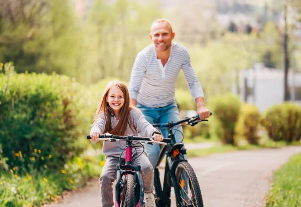 夏季户外骑自行车时 肖像带着女儿微笑的父亲 他们在夏季城市公园里聚精会神 快乐生儿育女或积极的体育生活概念形象 — 图库照片