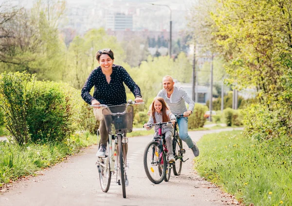 夏天外出骑自行车时 父母带着女儿微笑 他们在夏季城市公园里聚精会神 快乐生儿育女或积极的体育生活概念形象 — 图库照片