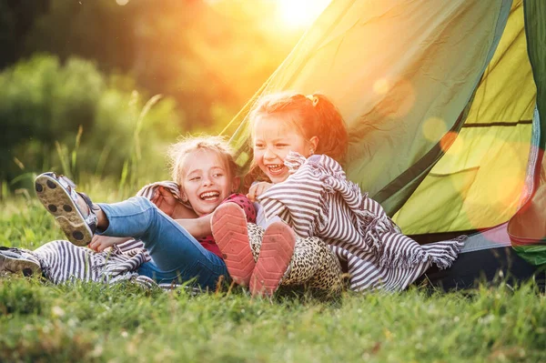 2人の女の子の妹は 緑の芝生のテントの入り口のキャンプの横に座って 陽気に冗談については お互いに語った笑っている 不注意な子供時代と屋外活動のコンセプト写真 — ストック写真