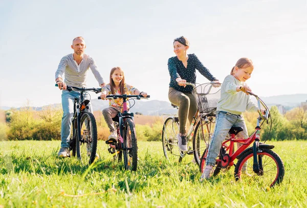 夏の屋外自転車に乗っている間に2人の娘と笑顔の父と母 彼らは緑の高い草の牧草地で一緒に楽しむ 幸せな親と子供時代やアクティブなスポーツライフコンセプトイメージ — ストック写真
