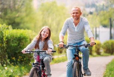 Yazın bisiklet sürerken kızıyla gülümseyen baba portreleri. Onlar yaz şehir parkında birliktelikten hoşlanırlar. Mutlu ebeveynlik ve çocukluk veya aktif spor hayatı konsepti imajı.