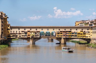Arno Nehri üzerindeki Ponte Vecchio köprüsünde eski Floransa kenti Toscana, İtalya 'da gündüz çekilmiş bir turistik tekne fotoğrafı var. Eski mimari yapılar benzersizdir ve en çok ziyaret edilen çekici turist manzarasıdır.