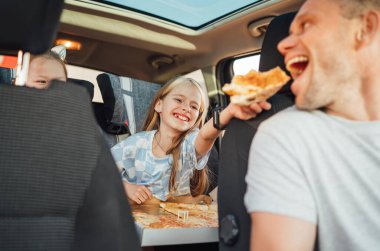 Olumlu gülümseyen kızın portresi çocuk koltuğunda otururken babasının ağzına pizza koyuyor. Mutlu çocukluk, fast-food yemek ya da otomobil Jorney yemek molası konsepti imajı