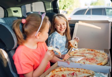 İki pozitif gülümseyen kız kardeşin portresi İtalyan pizzası pişiriyor çocuk oto koltuklarında oturuyor. Mutlu çocukluk, fast food yemek ya da otomobil Jorney yemek molası konsepti.