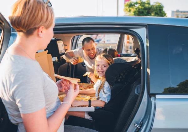 子供の車の座席で積極的な笑顔の女の子一方 家族の車の旅ブレーキだけでイタリアのピザを調理食べて停止します 幸せな家族の瞬間 子供時代 ファーストフードや自動車旅行のランチ休憩のコンセプトイメージ — ストック写真
