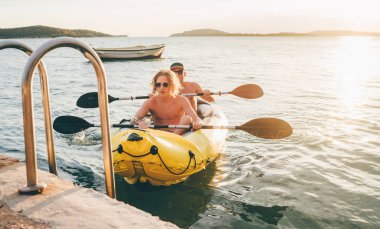 Father with teenager son on the bright yellow inflatable kayak returning back from evening ride by the Adriatic sea harbor in Croatia near from Sibenik city. Vacation and family values concept image.