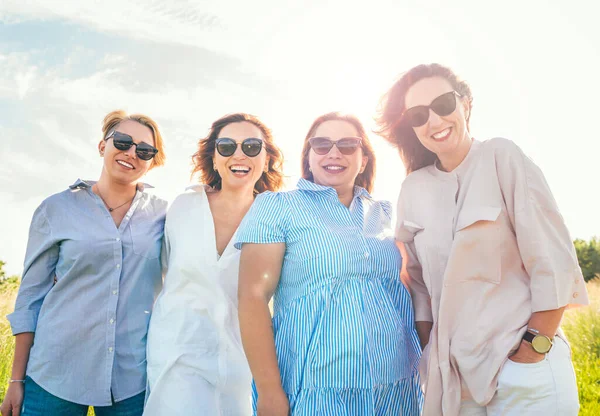 四个戴着太阳镜 笑容满面的女人在户外散步时拥抱并看着相机的画像 女人的友谊 关系和幸福的概念形象 — 图库照片