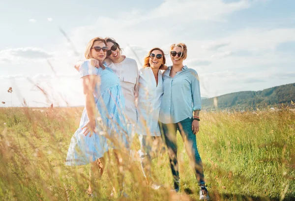 四个笑容可亲的女人在青草丘陵前散步时拥抱的画像 他们看着摄像机 妇女的友谊 关系和幸福概念形象 — 图库照片