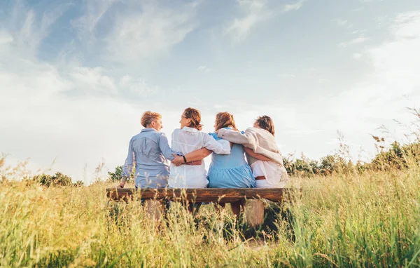 4人の笑顔の女性が屋外歩行中に牧草地のベンチに座って受け入れる光の夏服の害を着て 女性の友情 幸福の概念イメージ — ストック写真