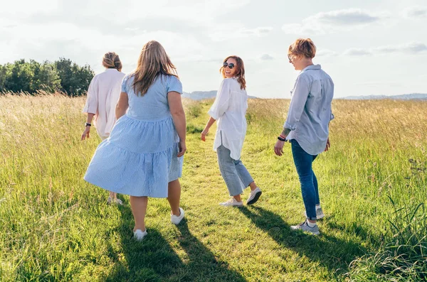 4つの明るい笑顔の女性は 高い緑の芝生の牧草地の丘を歩いて笑って 日没の散歩中にお互いにチャット 女性の友情 幸福の概念イメージ — ストック写真