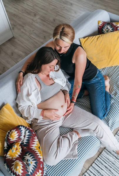 若い女はパートナーの妊婦の腹に触れる傾向がある 自宅のリビングルームで同性結婚のカップル 女性の健康 幸せな妊娠ドーラをサポートし 穏やかな精神的な気分の概念のイメージ — ストック写真