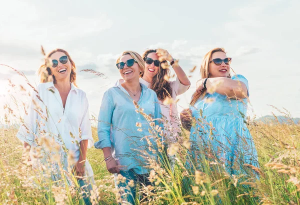 四个笑容可亲的女人在青草丘陵前散步时拥抱的画像 他们看着摄像机 妇女的友谊 关系和幸福概念形象 — 图库照片