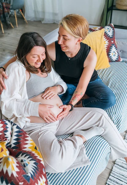 年轻女子轻柔触摸伴侣的女性怀孕腹部 同性伴侣在家里的客厅里 女人的健康 快乐的怀孕 支持和镇定的心理观念形象 — 图库照片