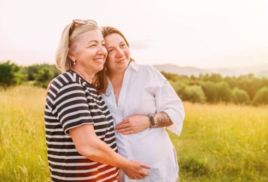 İçtenlikle gülümseyen genç bir kadının portresi. Hafif yaz kıyafetleri içinde. Akşam günbatımında annesiyle kucaklaşıyor. Kadın sağlığı, insan, doğa konsepti imajı..