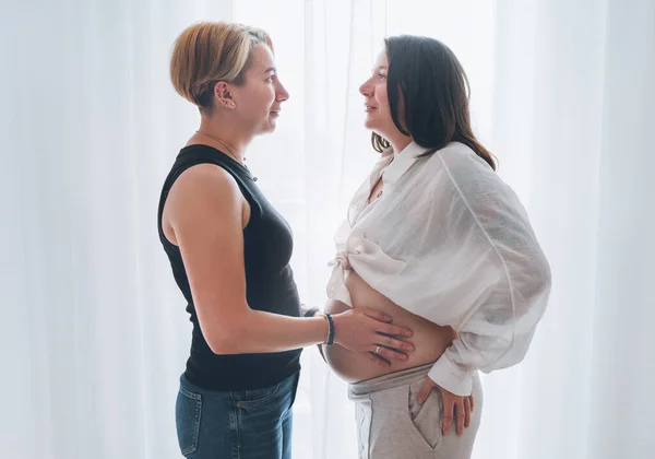 年轻女子轻柔触摸伴侣的女性怀孕腹部 同性伴侣在客厅窗户旁边 女人的健康 快乐的怀孕 支持和镇定的心理观念形象 — 图库照片