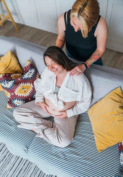 年轻女人温柔地按摩怀孕伴侣的女性肩膀 同性伴侣在家里客厅的沙发上 女人的健康 快乐的怀孕 支持和镇定的心理观念形象 — 图库照片