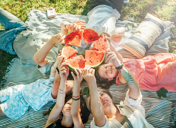 周末阳光明媚的日子 女儿们和父母一起躺在野餐毛毯上 微笑着 举起红色多汁的西瓜片 家庭价值观 水果维生素 户外时间观念 — 图库照片