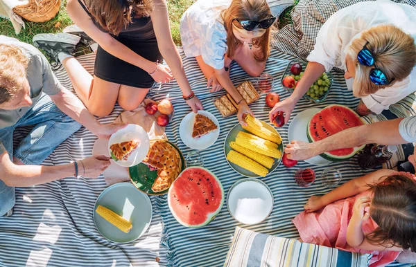 在城市公园里坐在野餐毛毯上的一家人的头像 他们正在吃煮熟的玉米 糕点和西瓜 家庭价值观和户外活动概念 — 图库照片