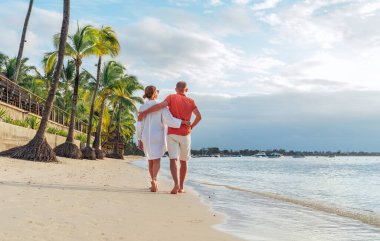 Couple in love hugging while walking on a sandy exotic beach. They have an evening walk by Trou-aux-Biches seashore on Mauritius island. People relationship and tropic honeymoon vacations concept