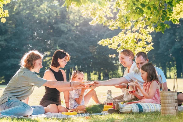 日曜日の晴れた日には 市内の公園のピクニックブランケットに座っている大きな家族 笑顔で冷たいお茶と一緒にパイを食べて笑っています 家族の価値観とアウトドア活動のコンセプト — ストック写真