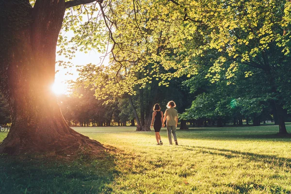 在夏城公园里 一个年轻的长发男孩和女友手牵着手在大树下散步 现代青少年关系观念形象 — 图库照片