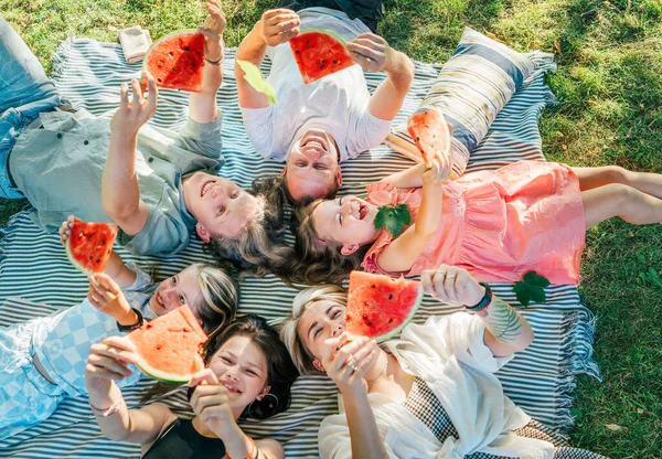 周末阳光明媚的日子 与父母团聚的女儿们躺在野餐毛毯上 笑着吃着红色多汁的西瓜片 家庭价值观 水果维生素 户外时间观念 — 图库照片