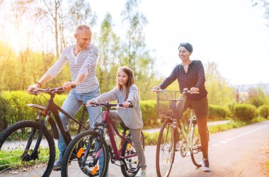 Yazın bisiklet sürerken kızıyla birlikte gülümseyen anne ve baba. Onlar yaz şehir parkında birliktelikten hoşlanırlar. Mutlu ebeveynlik ve çocukluk veya aktif spor hayatı konsepti imajı.