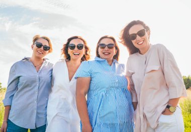 Güneş gözlüklü, kucaklaşan ve dışarıda yürürken kameraya bakan dört neşeli kadının portresi. Kadınların dostluğu, ilişkileri ve mutluluk konsepti imajı.