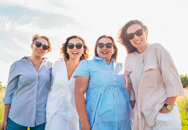 四个戴着太阳镜 笑容满面的女人在户外散步时拥抱并看着相机的画像 女人的友谊 关系和幸福的概念形象 — 图库照片