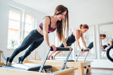 Spor spor salonundaki pilates reformatör spor aletini kullanarak uzun tahta statik kas güçlendirme egzersizi yapan iki genç bayan. Aktif insanlar eğitim, yoga dersleri konsepti. 