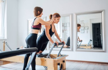 Genç bayan pilates eğitmeni sportif spor salonunda yenilikçi makina kullanarak ABS kas egzersizleri yaparak müşteri alımına yardımcı oluyor. Aktif insanlar eğitim, yoga dersleri konsepti.