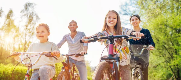 夏の屋外自転車に乗っている間に2人の娘と笑顔の父と母 彼らは夏の都市公園で一緒に楽しむ 幸せな親と子供時代やアクティブなスポーツライフコンセプトイメージ — ストック写真