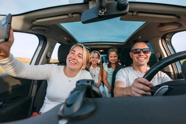 自動車の熱帯の間に車の中に2人の娘と幸せな若いカップル スマートフォンを使って笑ったり 笑ったり セルフィーを撮ったりしています 家族の価値観 ソーシャルメディア 新しいテクノロジーの概念 — ストック写真